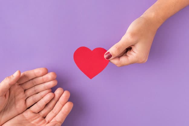 Un mano dando a otras un corazón de papel